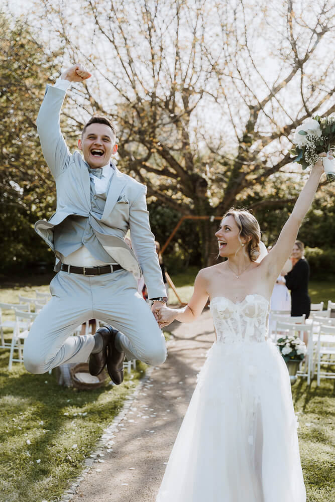 Bräutigam springt beim Auszug vor Freude in die Luft bei seiner Weingut Hochzeit in der Pfalz