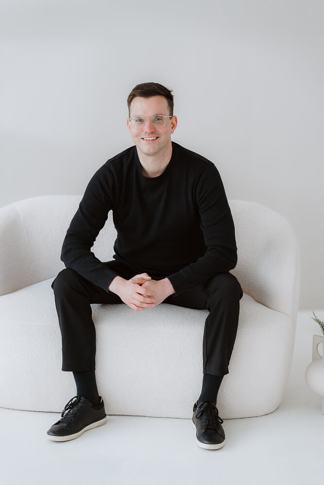 Hochzeitsfotograf sitzt auf Couch im Studio mit Blick in die Kamera